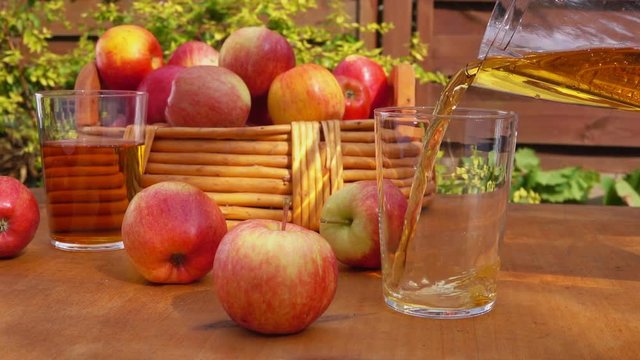 Apple juice and a basket of ripe apples on a wooden table. Slow motion.