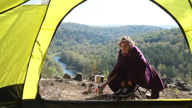 Young blonde woman tourist sitting on camping chair and drinking tea. Russia, Siberia, Salair
