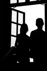 Silhouette of a girl and a boy walking up stairs. A big window in front of them. Black and white image.