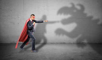 A superhero businessman fighting off a dragon shadow on concrete background.