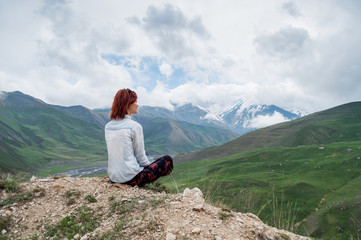 Female with red hairs enjoing stunning landscape of mountains. Dark clouds on the sky