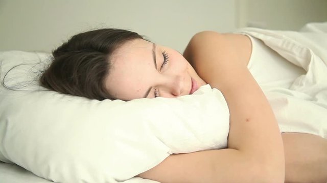 Young Beautiful Happy Adult Lady Sleeping Soundly On Bed In Bedroom At Home Or Hotel, Hugging White Comfy Pillow, Having Good Dream, Lying With Her Eyes Closed On Comfortable Mattress In Relaxed Pose