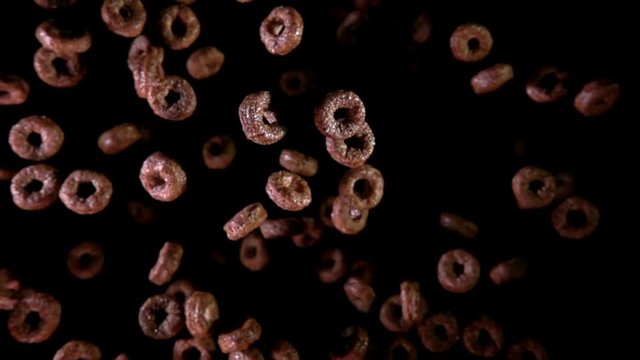 Crispy ringlets for breakfast fly to the camera on a dark background. Slow motion