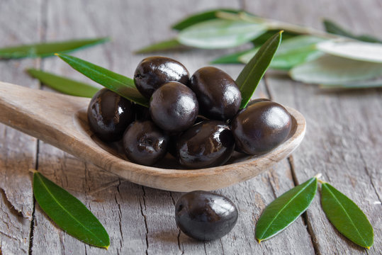 Black olives on wooden spoon with leaves