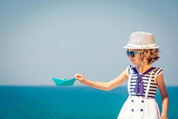 Child with paper sailing boat on summer vacation