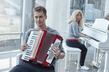 Portrait of young handsome Caucasian blue- eyed male playing accordion in a luxury house with...