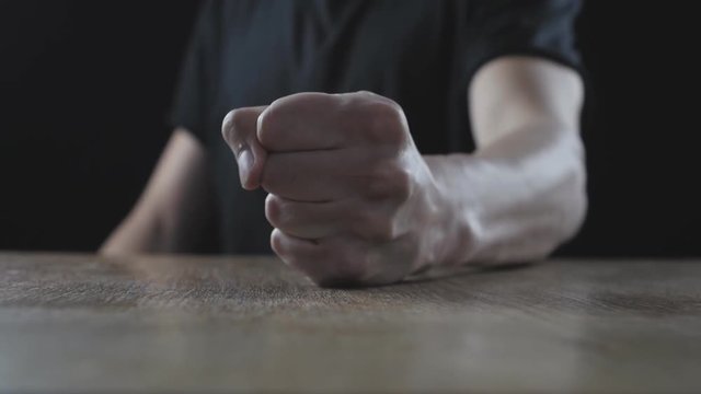 The concept of anger. The man beats his fist on the table showing aggression.