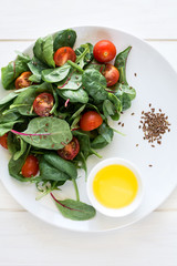 Fresh spring vegetarian salad with lettuce mix, cherry tomatoes, olive oil and flax seeds on white plate. Selective focus