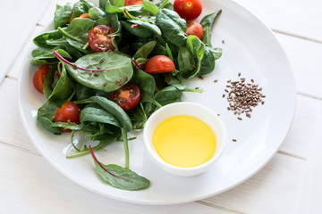 Fresh spring vegetarian salad with lettuce mix, cherry tomatoes, olive oil and flax seeds on white plate. Selective focus