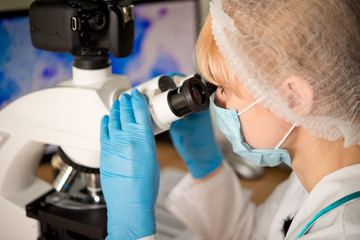 Laboratory assistant or technician in medical research lab looking into a microscope and doing research