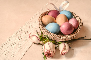 Dyed eggs with rose buds and satin bow in a wattled basket on white lace border
