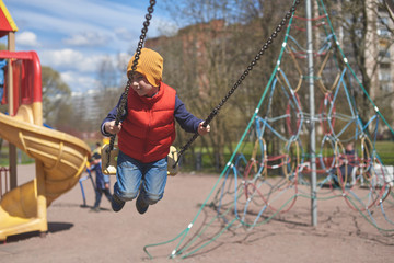 Cute European boy is swinging on children's playground.