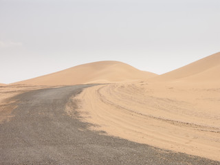 Fototapeta na wymiar desert road disappearing between two dunes