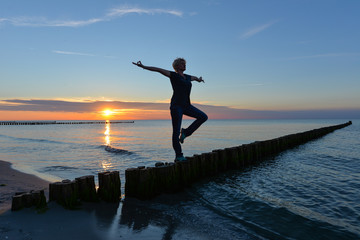 Fototapeta premium Frau macht Yoga im Sonnenuntergang am Meer