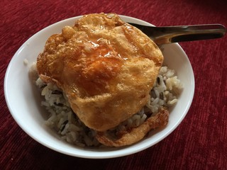 Fried egg over brown rice with shareing spoon, white bowl put on the red sofa