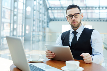 Serious leader with gadgets looking at camera by workplace