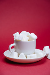 White cup full of sugar. No diet. Unhealthy concept. Sugar on red background.
