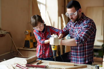 Little boy helping his father drill wooden plank together