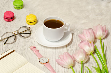 Coffee mug, sunglasses, watches, notebook and pink tulips on the table. Working concept. Top view