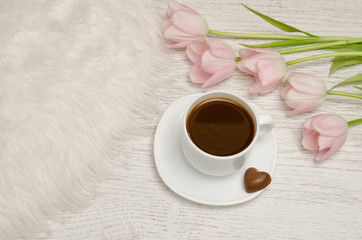 Coffee mug with candy and pink tulips on the table.
