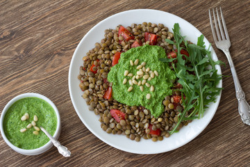 Homemade lentils with tomatoes and pesto sauce from arugula on a wooden background. Delicious healthy food