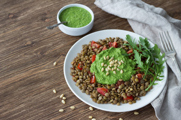 Homemade lentils with tomatoes and pesto sauce from arugula on a wooden background. Delicious healthy food