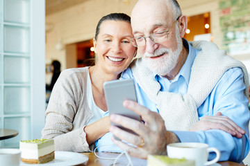 Affectionate couple with smartphone having nice leisure in cafe