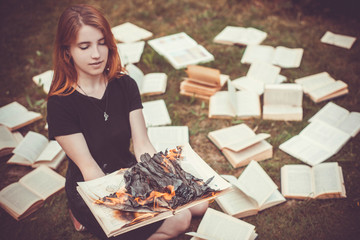 A girl holding a book burning in nature in summer garden