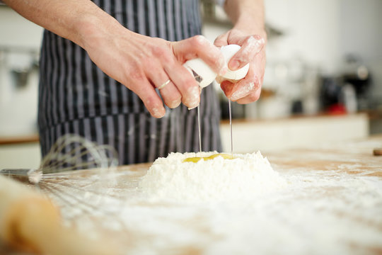 Baker breaking raw egg into wheaten flour