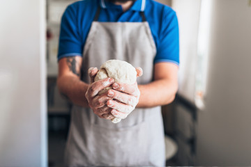 Male person in apron holds dough in hands