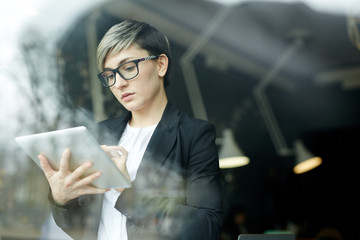 Portrait of young woman with creative haircut using digital tablet for planning work in office