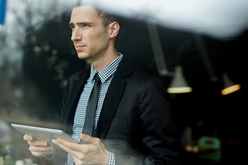 Portrait of young handsome businessman using digital tablet for  work in office looking away...
