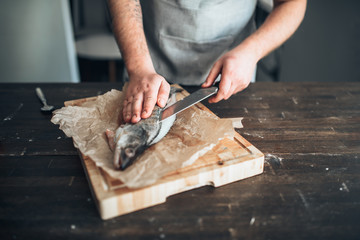 Fototapeta na wymiar Chef hands with knife cut up fish on cutting board