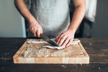 Fototapeta na wymiar Chef cuts raw fish slices on wooden cutting board