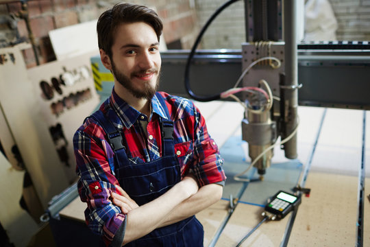 Portrait of handsome factory worker posing in workshop with machines and smiling to camera