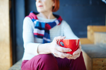 Red mug with hot drink in hands of relaxed senior woman
