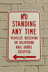 red and white No Standing Any Time sign on a painted white brick wall