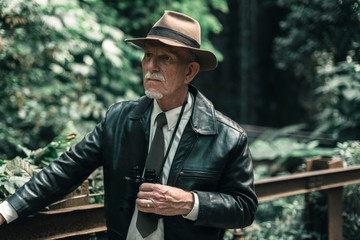 Explorer with hat and binoculars in jungle standing on bridge.