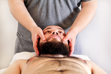 Fototapeta na wymiar Massage studio. Men hands masseuse for massage the head of a guy. Body care. Man having massage in the spa body massage salon. Massage table.
