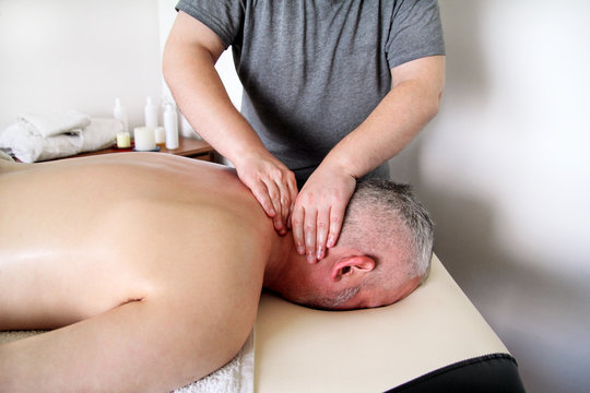 Sports massage studio. Massage therapist massaging shoulders of a male athlete, working with neck muscles. Body care. Man having massage in the massage salon. Massage neck muscles. Massage table.