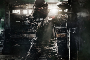 Fototapeta na wymiar Heavily armed masked paintball soldier on post apocalyptic background. Ad concept.