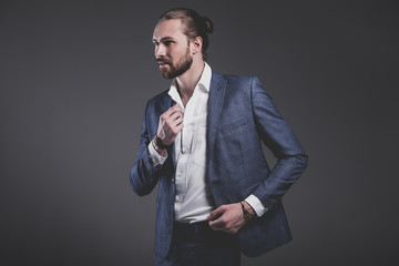 portrait of handsome fashion stylish hipster businessman model dressed in elegant blue suit posing on gray background in studio. Buttoning his jacket