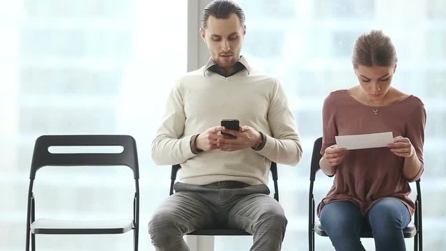 Scary employer at job search concept. Two young applicants waiting their turn for job interview or exam on chairs, feeling nervous after looking at scared lady candidate running out after interview