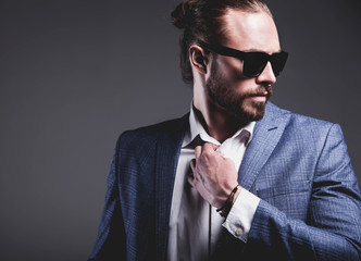 portrait of handsome fashion stylish hipster businessman model dressed in elegant blue suit in sunglasses posing on gray background in studio