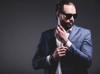 portrait of handsome fashion stylish hipster businessman model dressed in elegant blue suit posing on gray background in studio. Buttoning his jacket