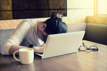 Asian charming beautiful girl worker sleeping with laptop and a cup of coffee in modern working room or coffee shop after work hard and stress. Break Digital device concept.