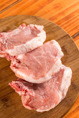 Raw pork chops on the round wooden background.