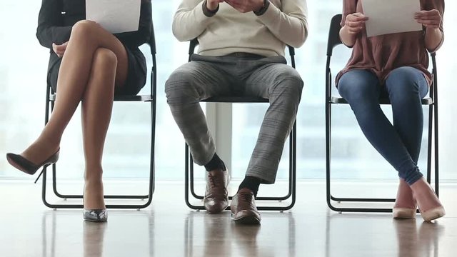 Ready to get new career. Group of three young businesspeople sitting on chairs in office, waiting and going for job interview, feeling nervous. Body language. Close up of legs. Job search concept