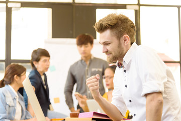 Fototapeta premium Smart handsome european man business officer celebrate after his jobs was successful and his project team in modern office and blurred multi ethnic business person group in casual suit in background. 