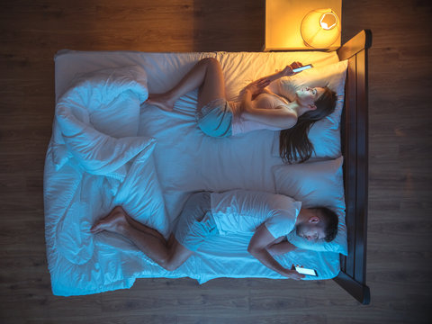 The unhappy couple with smartphone lay on the bed. night time. view from above